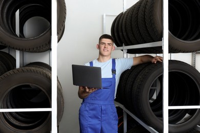 Smiling young man with laptop near car tires in auto store