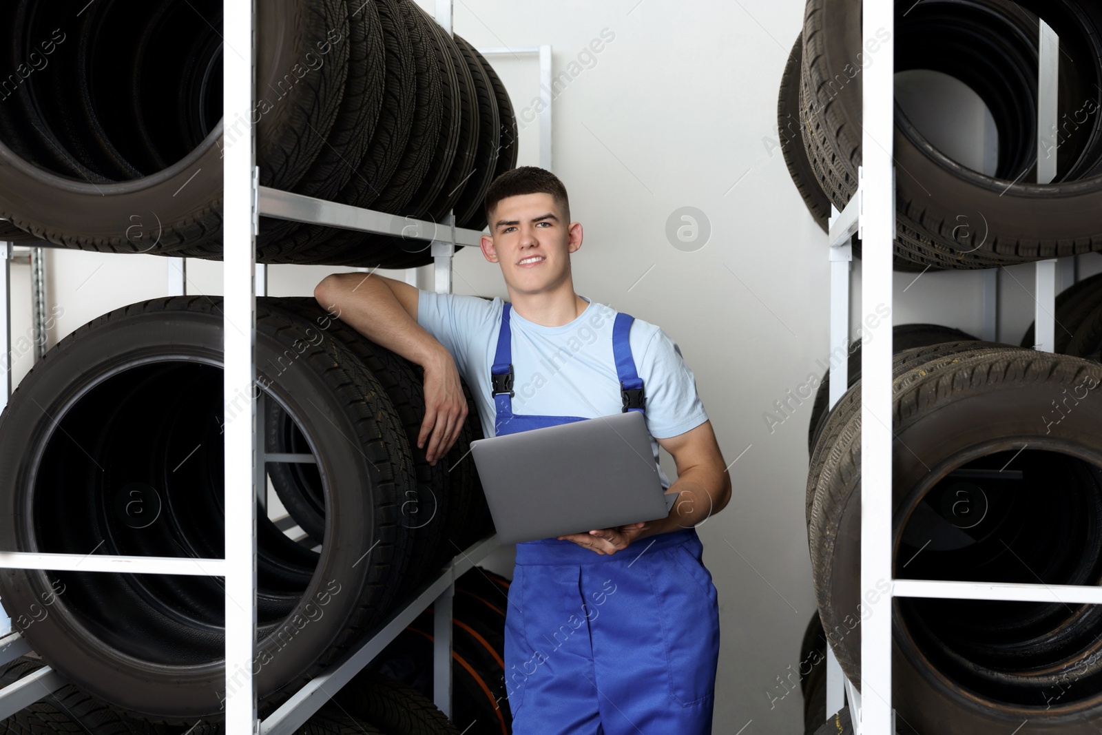 Photo of Smiling young man with laptop near car tires in auto store