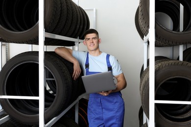 Smiling young man with laptop near car tires in auto store