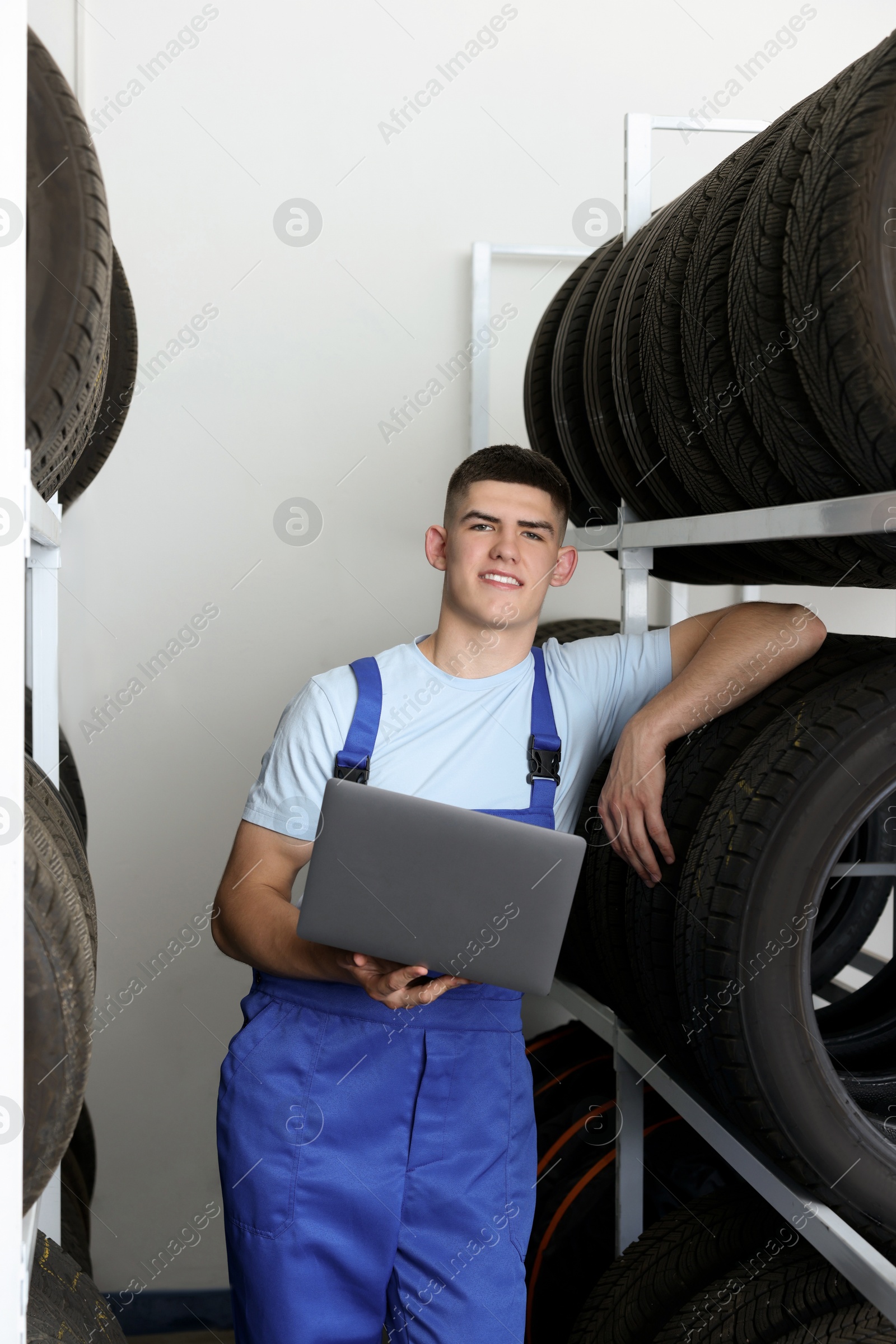 Photo of Smiling young man with laptop near car tires in auto store