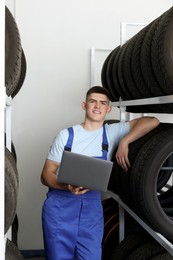 Smiling young man with laptop near car tires in auto store