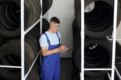 Young man with clipboard taking notes near car tires in auto store