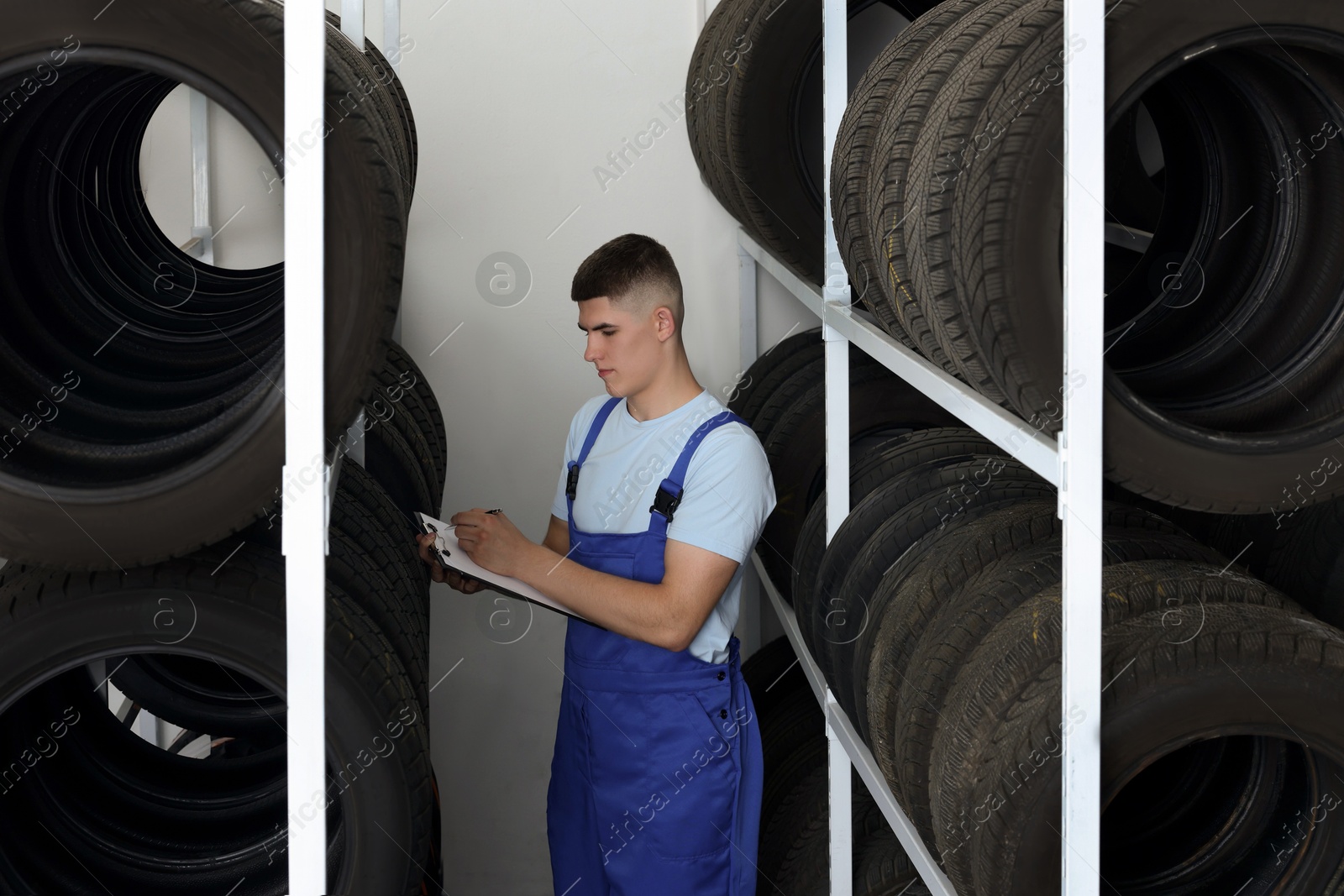 Photo of Young man with clipboard taking notes near car tires in auto store