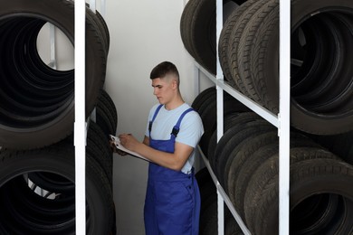 Young man with clipboard taking notes near car tires in auto store