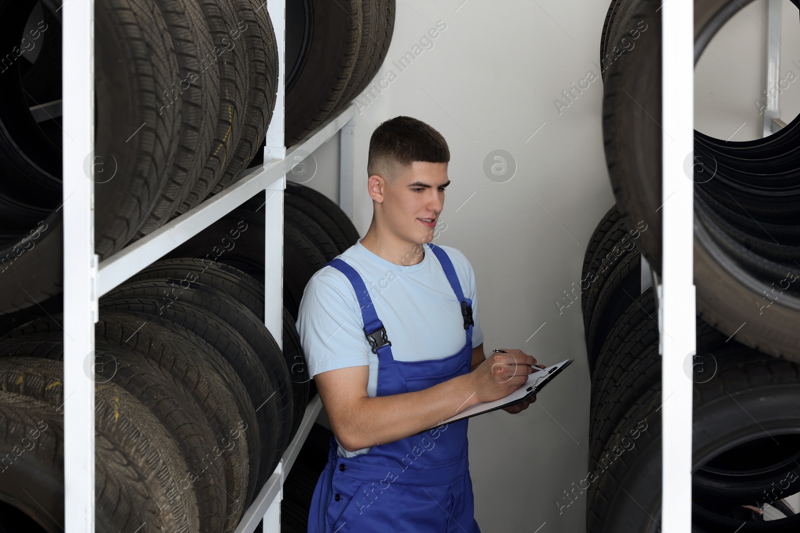 Photo of Young man with clipboard taking notes near car tires in auto store