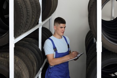 Young man with clipboard taking notes near car tires in auto store