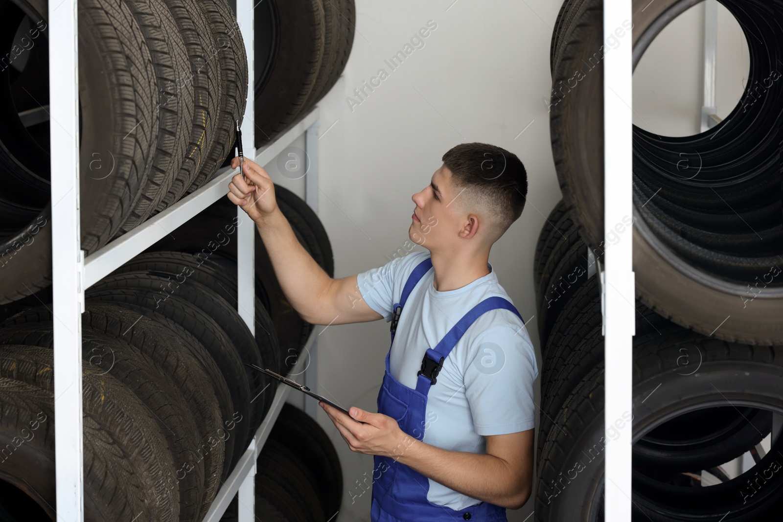 Photo of Young man with clipboard near car tires in auto store