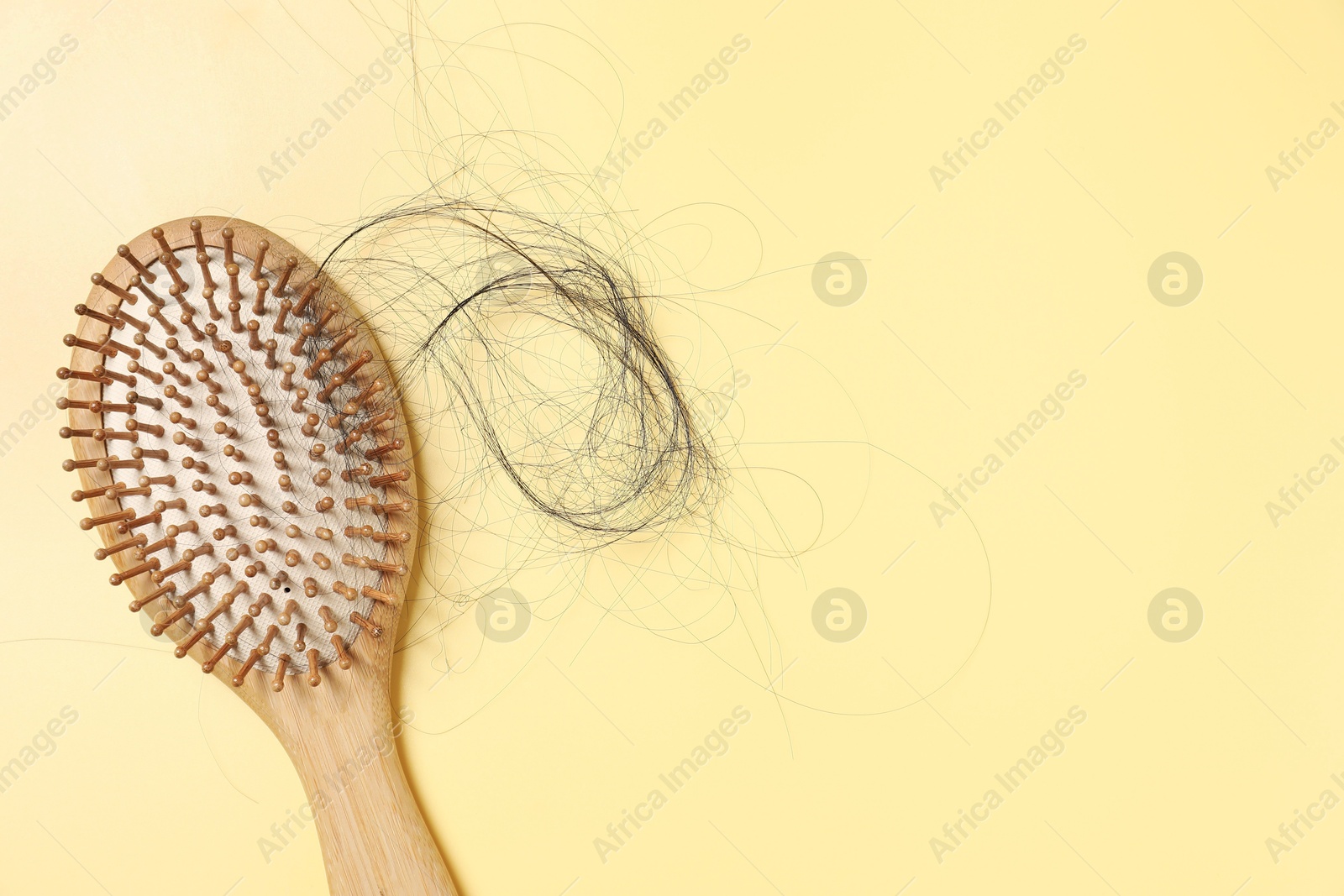 Photo of Wooden brush with lost hair on yellow background, top view. Space for text