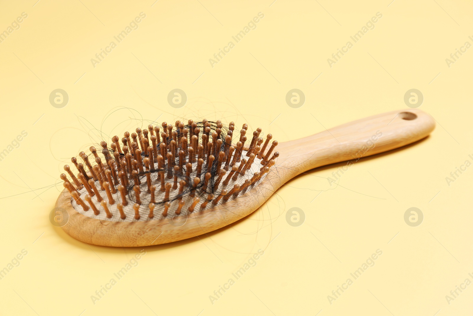 Photo of Wooden brush with lost hair on yellow background