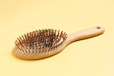 Photo of Wooden brush with lost hair on yellow background