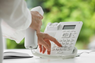 Photo of Assistant dialing number on telephone against blurred green background, closeup