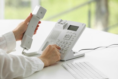 Photo of Assistant dialing number on telephone against blurred background, closeup