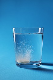 Effervescent pill dissolving in glass of water on light blue background