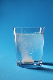 Effervescent pill dissolving in glass of water on light blue background