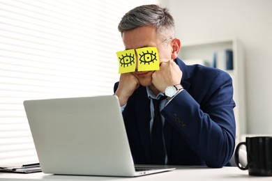 Man with fake eyes painted on sticky notes snoozing at workplace in office