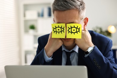 Man with fake eyes painted on sticky notes snoozing at workplace in office