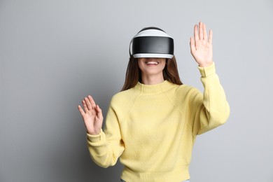 Photo of Smiling woman using virtual reality headset on light grey background