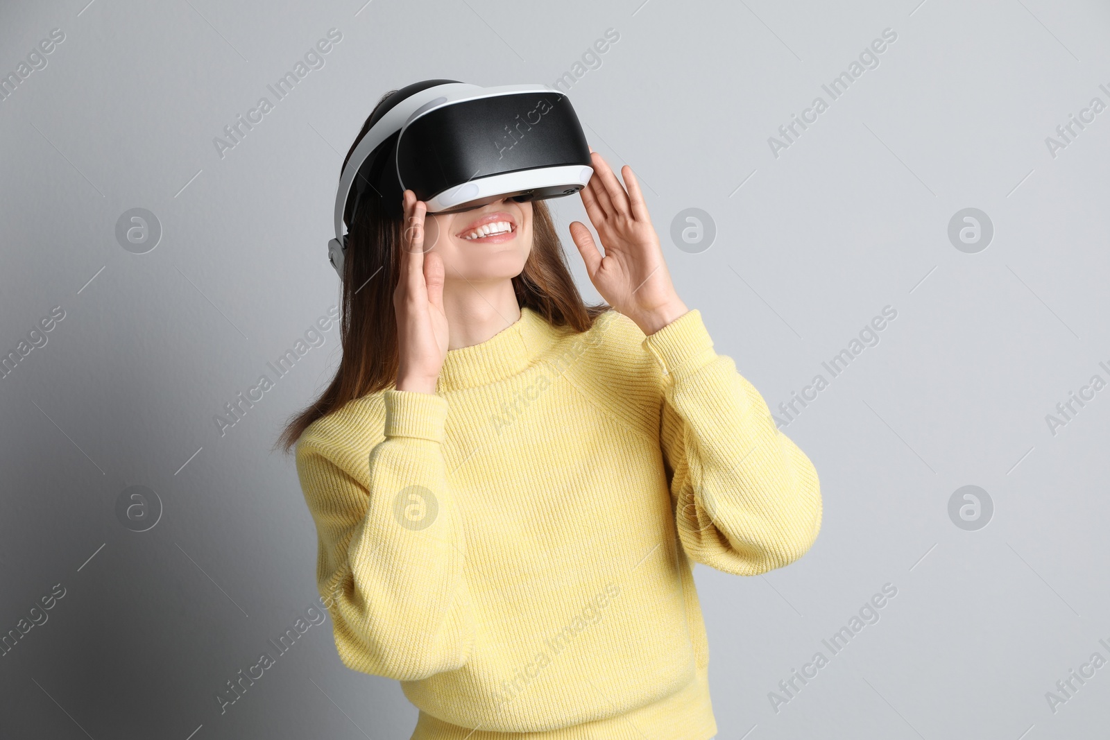 Photo of Smiling woman using virtual reality headset on light grey background