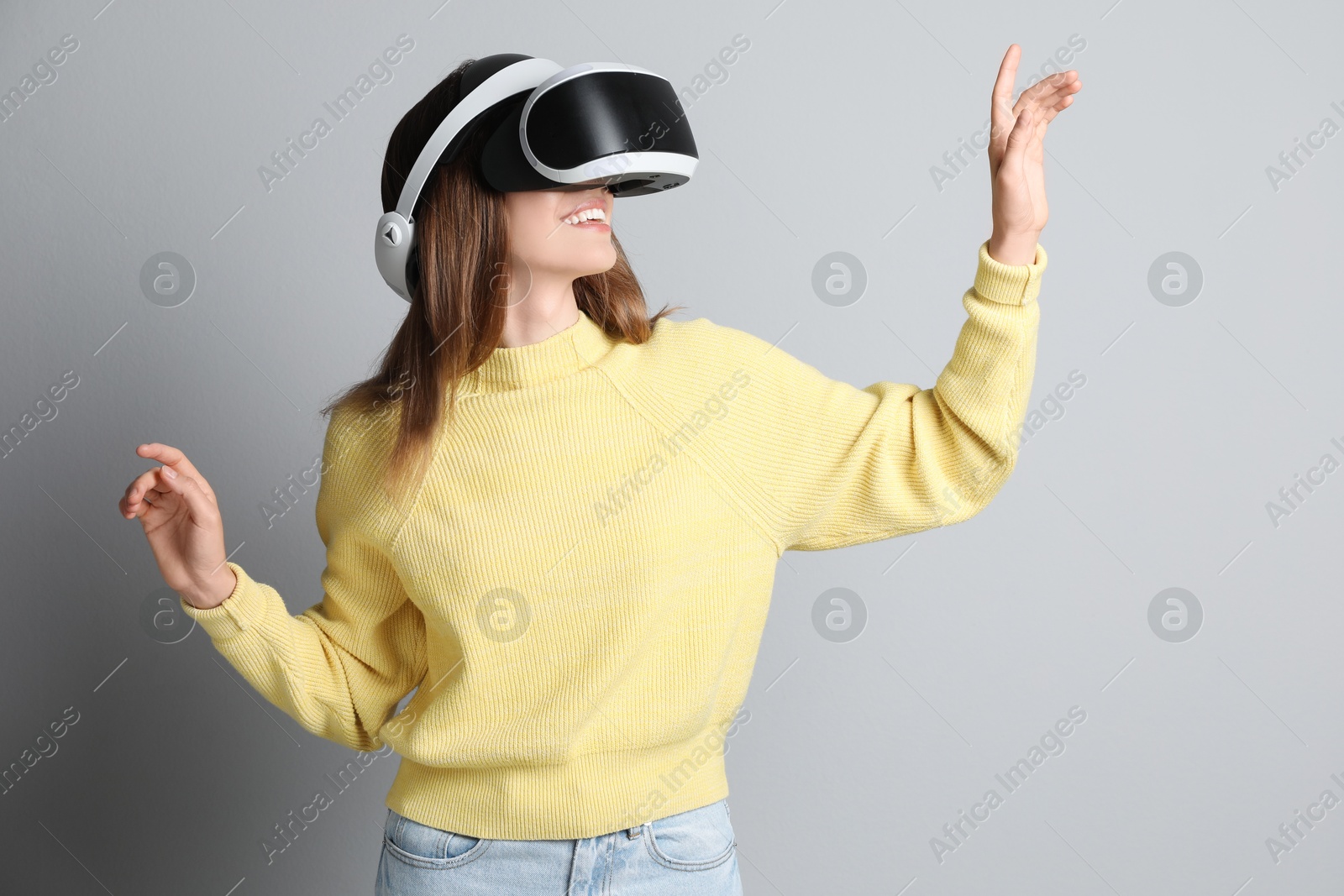 Photo of Smiling woman using virtual reality headset on light grey background