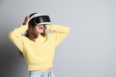 Smiling woman using virtual reality headset on light grey background. Space for text