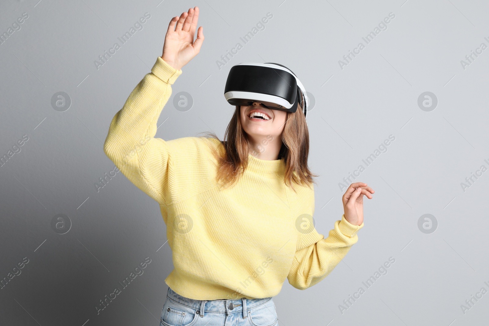 Photo of Happy woman using virtual reality headset on light grey background