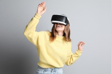 Photo of Happy woman using virtual reality headset on light grey background