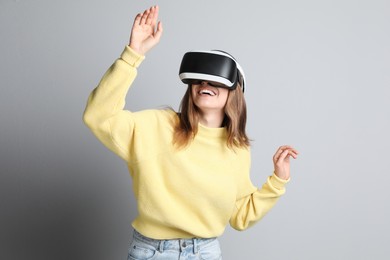 Happy woman using virtual reality headset on light grey background