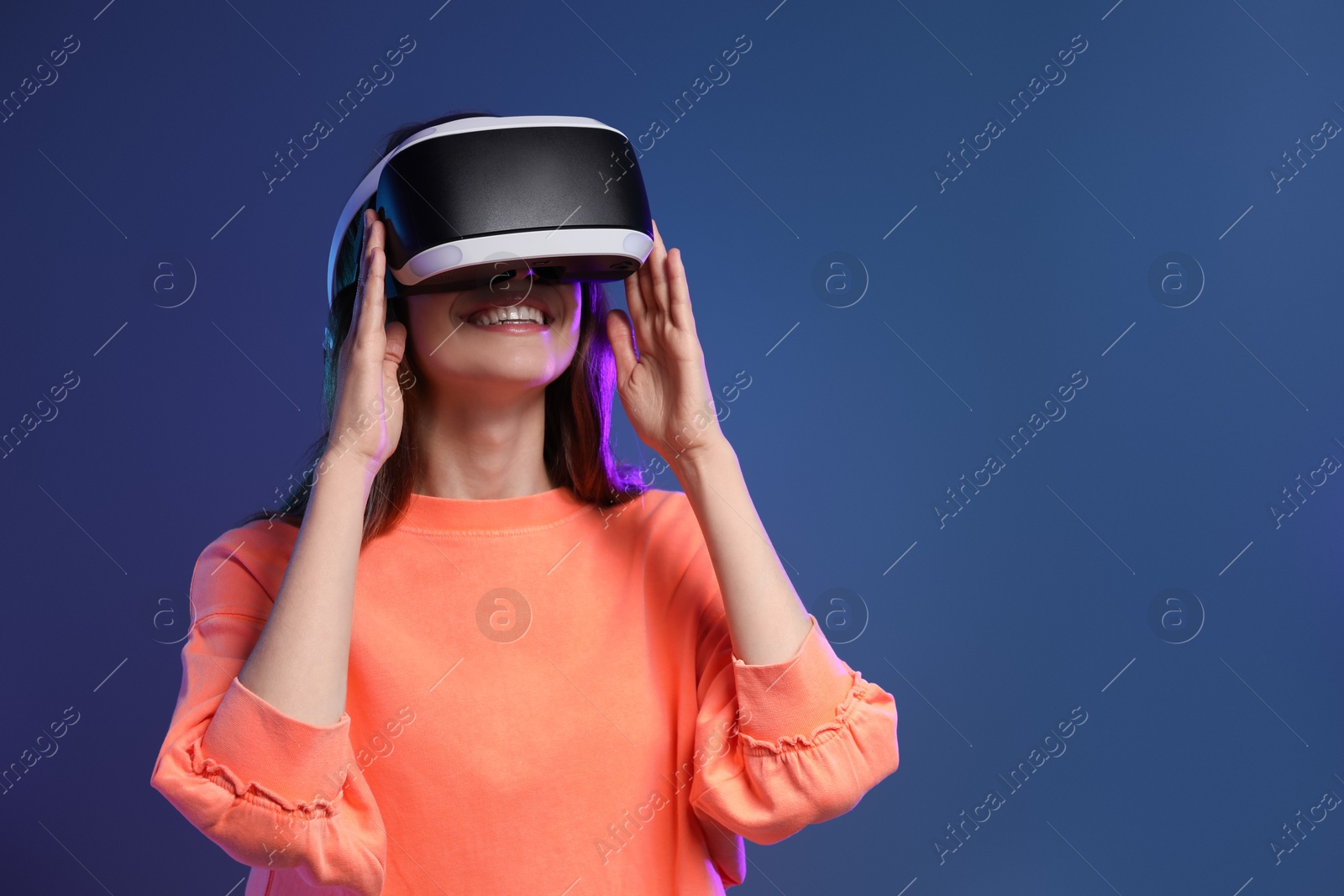 Photo of Smiling woman using virtual reality headset on dark blue background