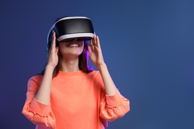 Photo of Smiling woman using virtual reality headset on dark blue background