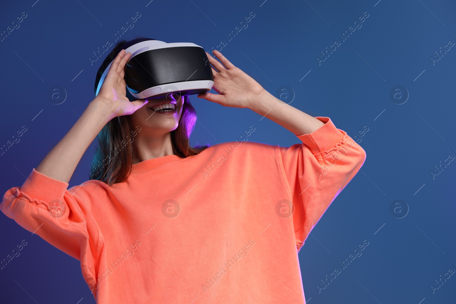 Photo of Smiling woman using virtual reality headset on dark blue background