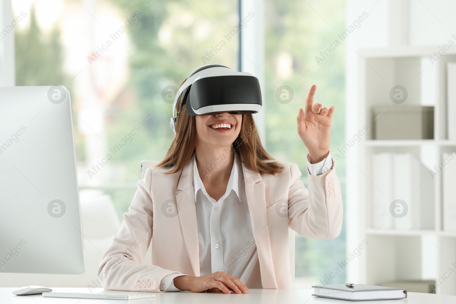 Photo of Smiling woman using virtual reality headset at workplace in office