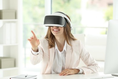 Photo of Smiling woman using virtual reality headset at workplace in office