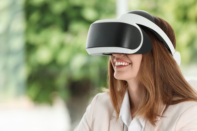 Photo of Smiling woman using virtual reality headset indoors. Space for text