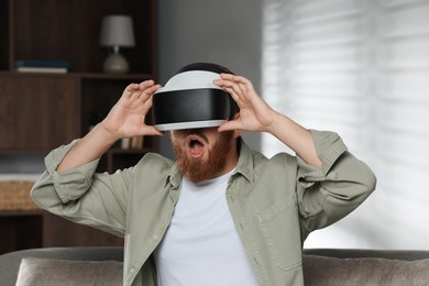 Photo of Emotional man using virtual reality headset on sofa at home