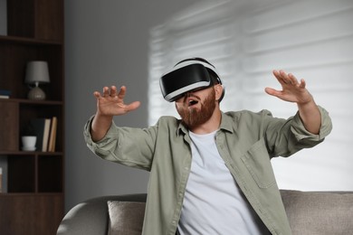 Photo of Emotional man using virtual reality headset on sofa at home
