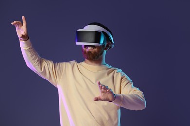 Photo of Smiling man using virtual reality headset on dark purple background