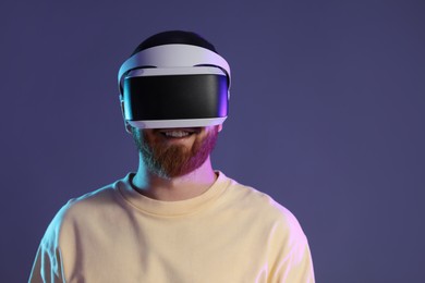 Photo of Smiling man using virtual reality headset on dark purple background. Space for text