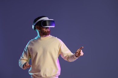 Photo of Man using virtual reality headset on dark purple background. Space for text