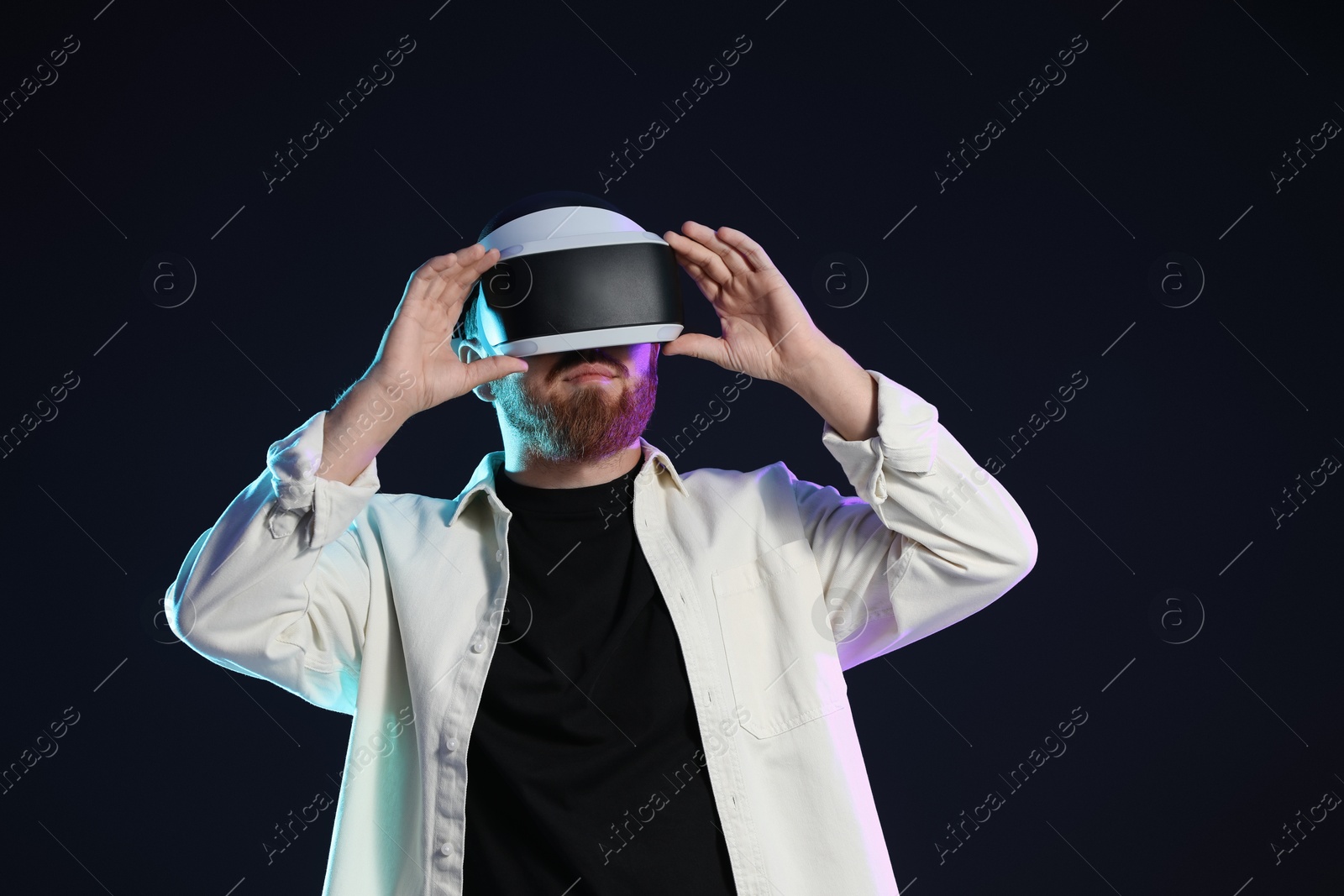 Photo of Man using virtual reality headset on dark background in neon lights