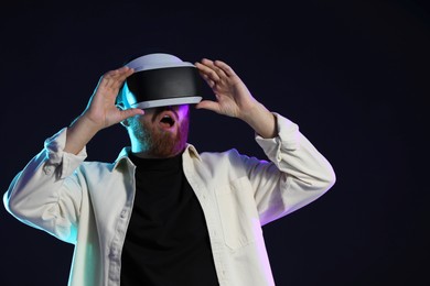 Photo of Emotional man using virtual reality headset on dark background in neon lights. Space for text