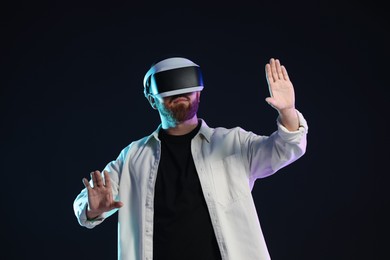 Photo of Man using virtual reality headset on dark background in neon lights