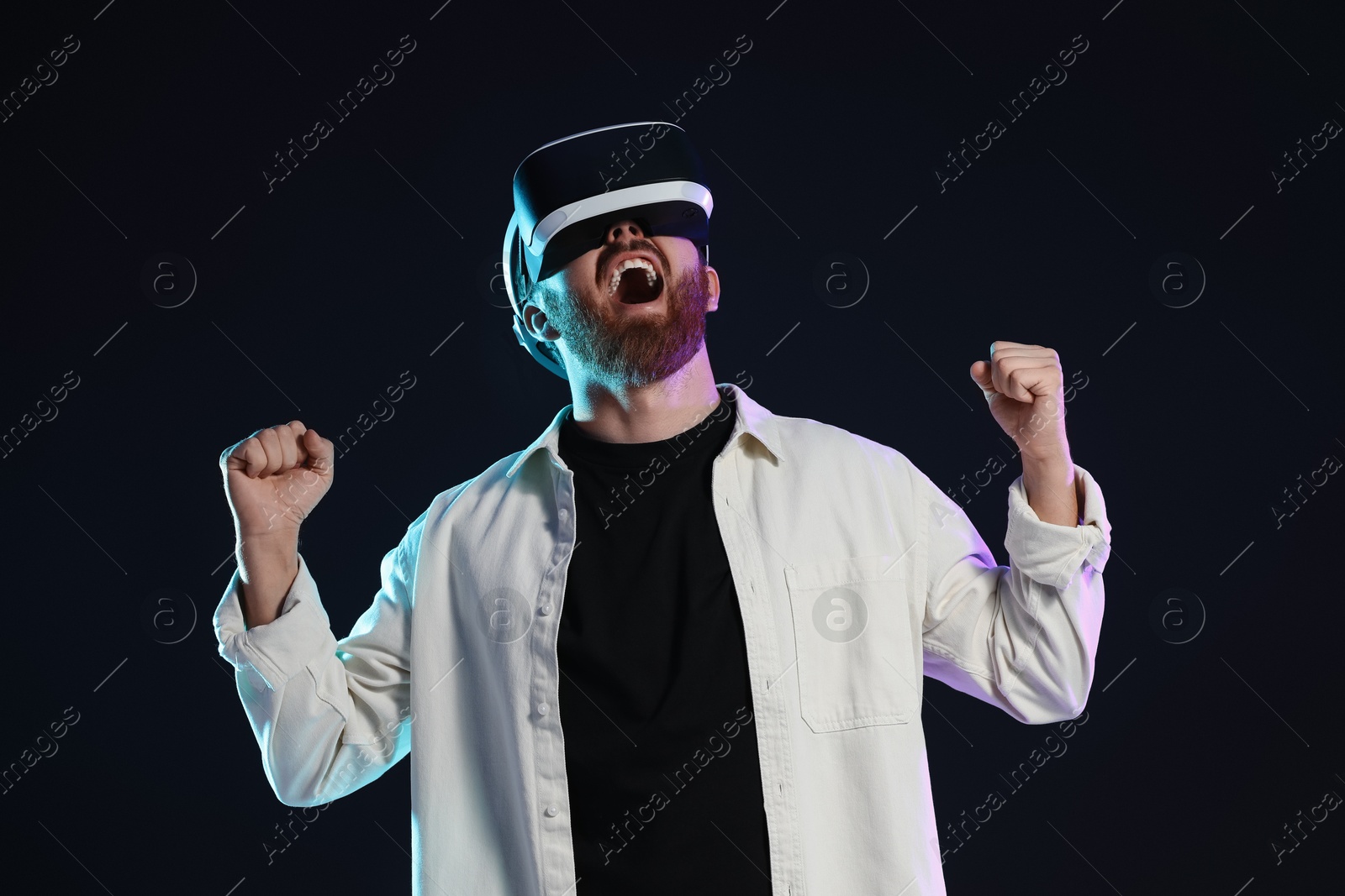 Photo of Emotional man using virtual reality headset on dark background in neon lights