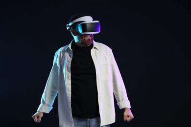 Photo of Man using virtual reality headset on dark background in neon lights