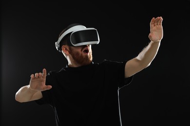 Photo of Emotional man using virtual reality headset on black background