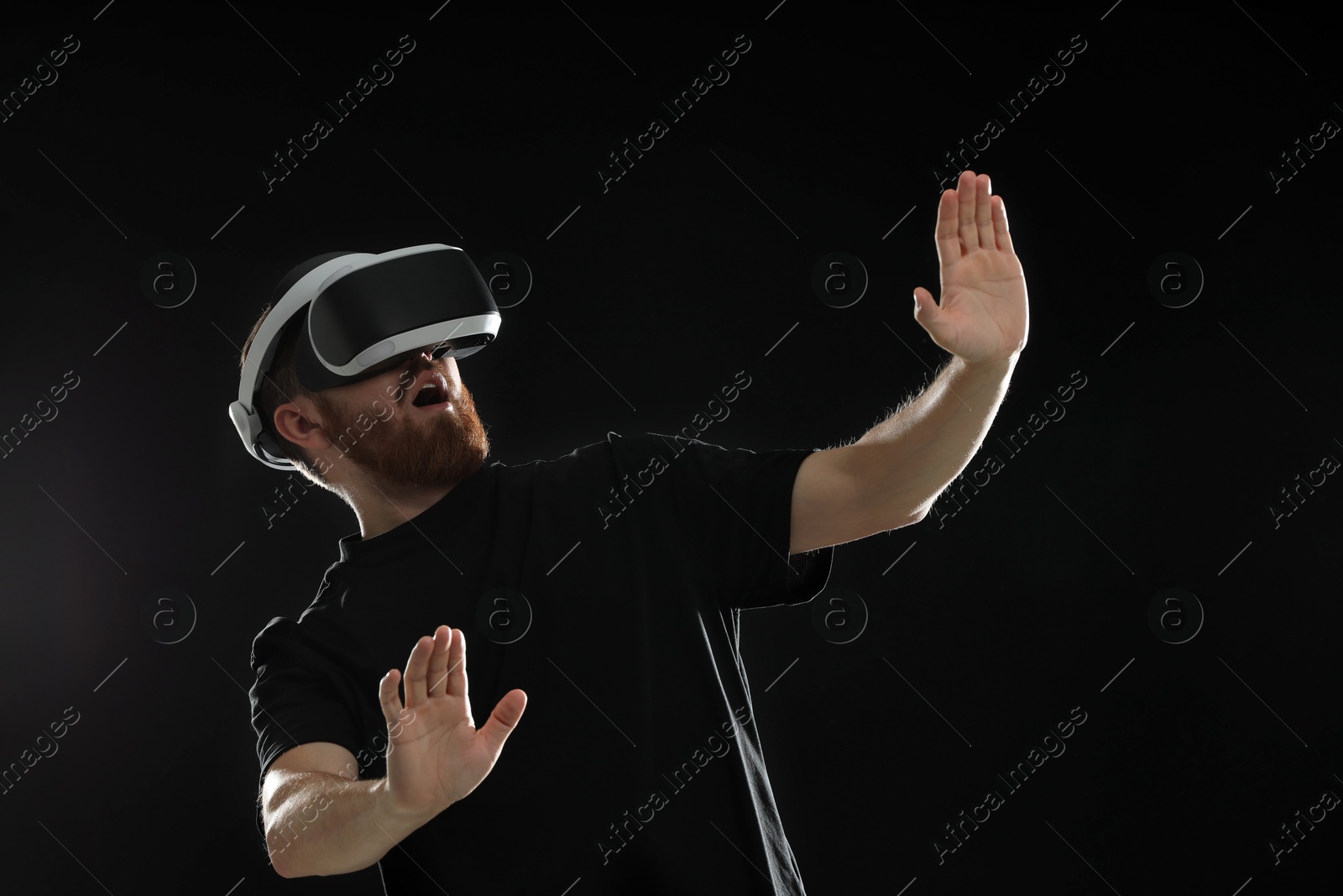 Photo of Emotional man using virtual reality headset on black background