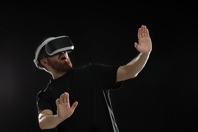 Photo of Emotional man using virtual reality headset on black background