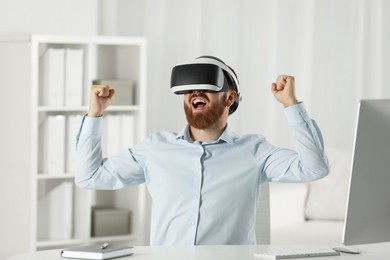 Photo of Emotional man using virtual reality headset at workplace in office