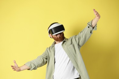 Photo of Happy man using virtual reality headset on pale yellow background