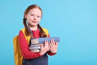 Cute little girl with stack of books on light blue background. Space for text