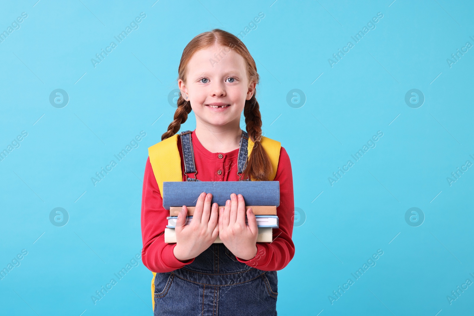 Photo of Smiling little girl with stack of books on light blue background